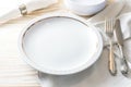 Preparation for a place setting with a white plate, napkin and nostalgic silver cutlery on a light-colored wooden table for