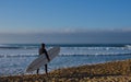 Isolated surfer walking along the shoreline with surfboard under his arm and watching the ocean waves in the early morning hours. Royalty Free Stock Photo