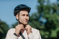 Preparation for ride to bicycle in city. Handsome young man in shirt puts on safety helmet Royalty Free Stock Photo