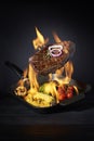 Preparation steak and vegetables in pan with fire flame on dark background. Restaurant and hotel service concept. Restaurant and