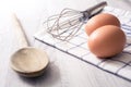 Prepare Breakfast Eggs Concept With 2 Eggs, A Wooden Spoon, An Eggbeater And A Towel On A Kitchen Table