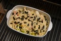Prepared endives or chicory gratin with apple, ham, cheese and pumpkin seeds in a casserole on a baking grid ready for the oven