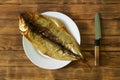 Prepared smoked Baikal omul in a white plate next to a knife on a wooden rustic table made of pine boards. A rare fish delicacy -