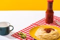 Prepared spaghetti with tomato sauce beside cup on white surface on yellow background