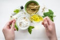 Preparing an alternative medicine, herbal extract: white background, hands hold a jar of oil over a bowl with white essence, and Royalty Free Stock Photo