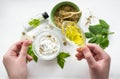 Preparing an alternative medicine, herbal extract: white background, hands hold a jar of oil over a bowl with white essence, and Royalty Free Stock Photo