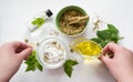 Preparing an alternative medicine, herbal extract: white background, hands hold a jar of oil over a bowl with white essence, and Royalty Free Stock Photo