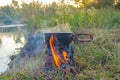 Preparing breakfast or tourist morning coffee in camp kitchen fry pan or skillet on portable stove, which burned wood chips on riv