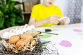 Preparing for Easter. In the foreground is a nest with eggs, in the background in the focus the child is engaged in crafts for the