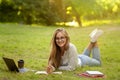 Preparing for exams outdoors. Smiling student girl reading book and taking notes Royalty Free Stock Photo