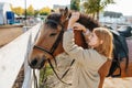 Preparing her horse for the ride, ginger girl putting on bridle on horse Royalty Free Stock Photo