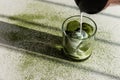 Pouring milk into glass with matcha green tea ice on white table sprinkled with matcha powder and strong shadows Royalty Free Stock Photo