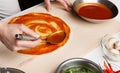 Preparing pizza. Chef spreading tomato sauce in pizzeria