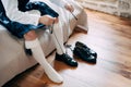 Preparing for a Scottish wedding. Man in a kilt, sporran and high socks sits on the bed and tie long shoelaces on his