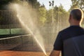 Preparing a tennis court for the match. A man is watering a field with a hose