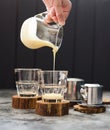 Preparing Vietnamese pour over coffee. Woman hand pouring condensed milk into glasses on dark background