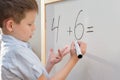 A preschool-age boy with a funny facial expression stands at a white board and decides an example in mathematics. The