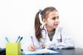 Preschool age girl playing doctror character, white lab coat, sitting at the desk, white background