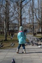 Preschool-aged girl in a blue jacket twirls around herself in front of a flock of city doves. Portrait of a five-year-old child