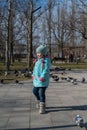 Preschool-aged girl in a blue jacket twirls around herself in front of a flock of city doves. Portrait of a five-year-old child