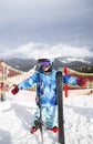 preschool boy in helmet, blue overalls, ski boots stands in snow on top of mountains, holds skis Royalty Free Stock Photo