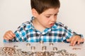 A preschool boy in a plaid shirt counts coins, builds towers. Financial literacy for children.