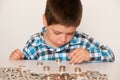 A preschool boy in a plaid shirt counts coins, builds towers. Financial literacy for children.