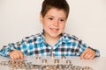 A preschool boy in a plaid shirt counts coins, builds towers. Financial literacy for children.