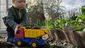 Preschool boy playing with a toy truck between the beds in the garden. Royalty Free Stock Photo