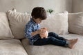 Preschool boy sit on sofa throw coins into piggy bank Royalty Free Stock Photo