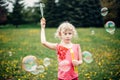 Preschool Caucasian blonde girl blowing soap bubbles in park on summer day. Child having fun outdoors. Authentic happy childhood Royalty Free Stock Photo