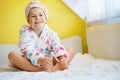 Preschool child after bath. Cute little girl with wet curly hair wearing a bathrobe and head towel sitting on bed Royalty Free Stock Photo