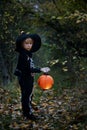 Preschool child with halloween costume and jack` o` lantern in a forest, scary skelleton