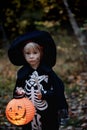 Preschool child with halloween costume and jack` o` lantern in a forest, scary skelleton