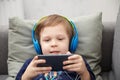 Preschool child listens to music on a smartphone while lying at home on the bed, boy plays on the phone Royalty Free Stock Photo