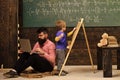 Preschool education. Arithmetic lesson at school. Kid writing on chalkboard while concentrated teacher works on laptop Royalty Free Stock Photo