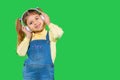 Preschool girl happily posing in big headphones on green background with empty side space. Royalty Free Stock Photo