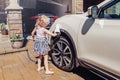 Preschool little Caucasian girl washing car on driveway in front house on sunny summer day Royalty Free Stock Photo