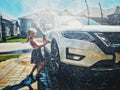 Preschool little Caucasian girl washing car on driveway in front house on sunny summer day Royalty Free Stock Photo