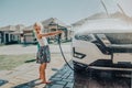 preschool little Caucasian girl washing car on driveway in front house on sunny summer day Royalty Free Stock Photo