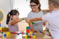 Preschool teacher with children playing with colorful wooden didactic toys at kindergarten