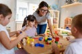 Preschool teacher with children playing with colorful wooden didactic toys at kindergarten