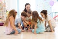 Preschool teacher plays with group of kids sitting on a floor at kindergarten