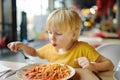 Preschooler boy eating pasta with tomatoes in cafe or restaurant. Healthy/unhealthy food for little kids