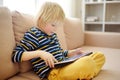 Preschooler boy learning on distance by digital tablet or playing computer game sitting on couch at home. Little child watching Royalty Free Stock Photo