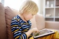 Preschooler boy is learning on distance by tablet or playing pc game sitting on couch. Homeschool education and entertainments for