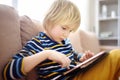 Preschooler boy is learning on distance by tablet or playing pc game sitting on couch. Homeschool education and entertainments for