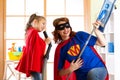 Preschooler girl and her mother dressed like superheroes. Middle-aged woman and kid playing while doing cleanup at home