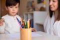 Preschooler kid drawing with coloured pencils with mother or teacher educator. Focus on the pencils. Homeschooling. Learning