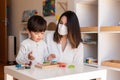 Preschooler Kid playing tetris wood puzzle with teacher educador help using face mask for coronavirus pandemic. Homeshooling.